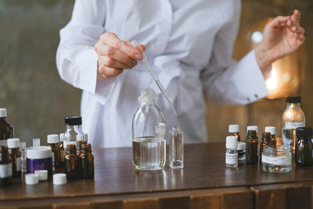 Person in lab coat using dropper to transfer liquid into clear glass bottles on a table.