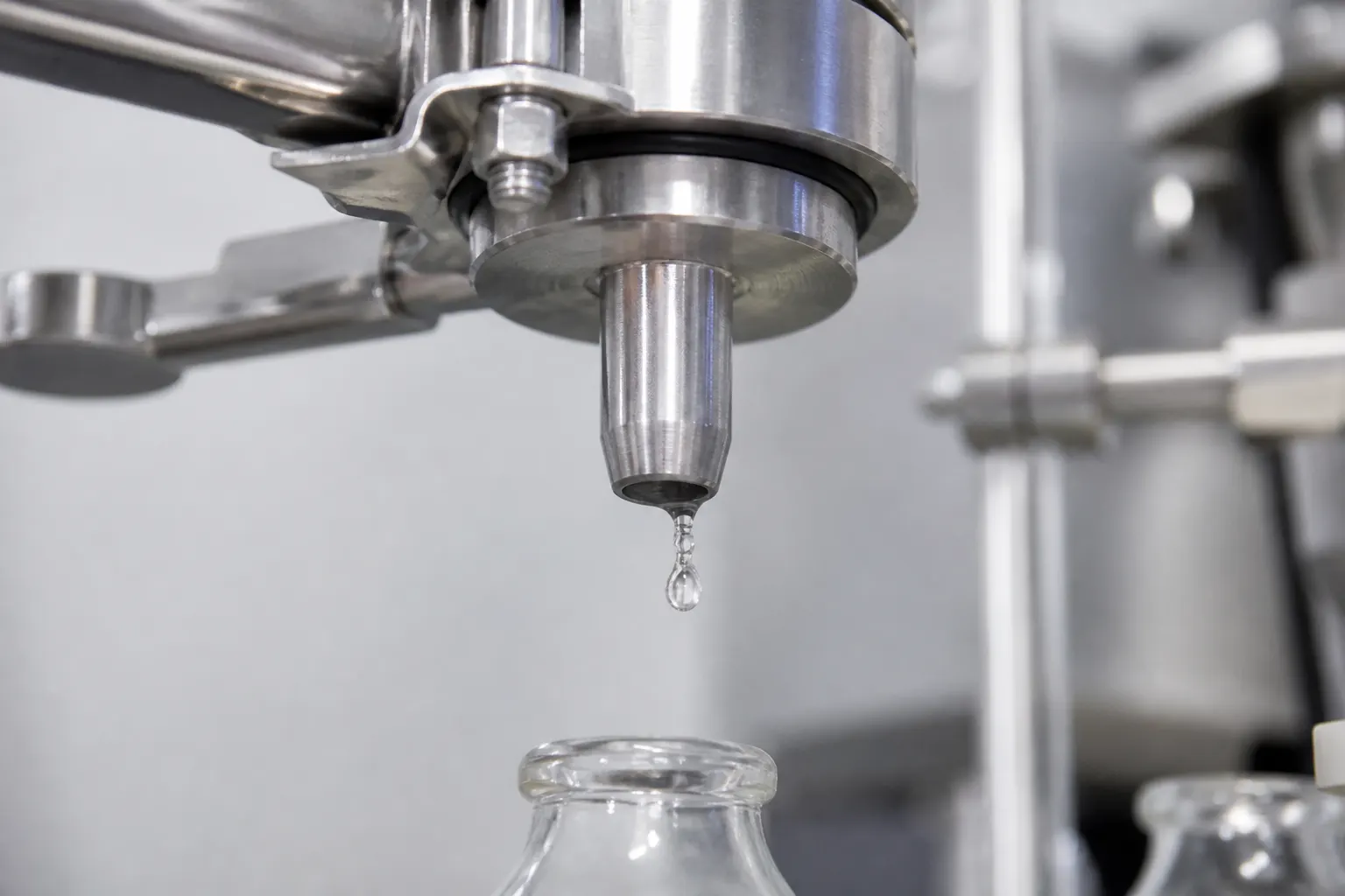 Stainless-steel filling nozzle releasing a liquid droplet into a glass bottle on the filling station